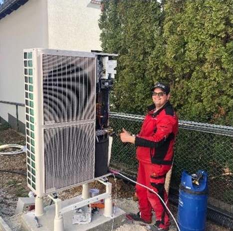 A Valerian Klíma szerelője piros munkaruhában egy hőszivattyú kültéri egysége mellett