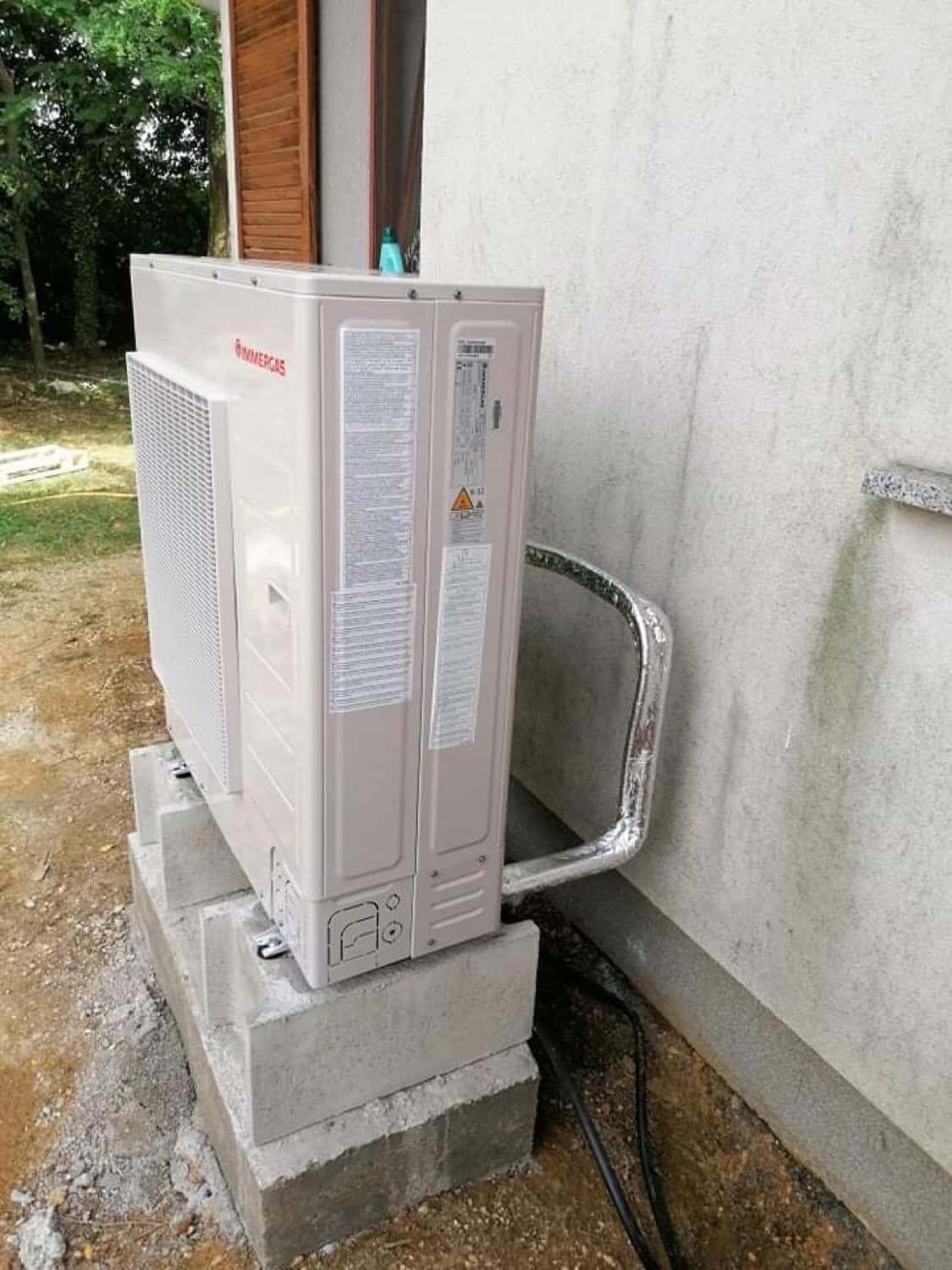 Hőszivattyú kültéri egysége betonalapon, a ház fala mellett